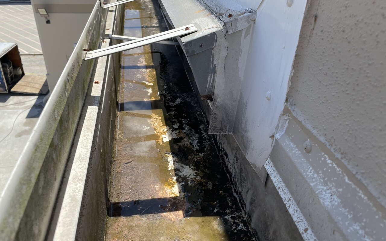 A grimy commercial roof gutter and trough before cleaning